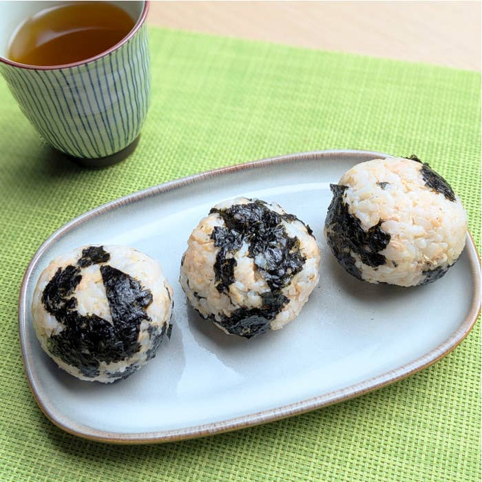 おにぎりが3つ、楕円形の皿に乗っている。隣にお茶が入った湯呑みが置かれている。