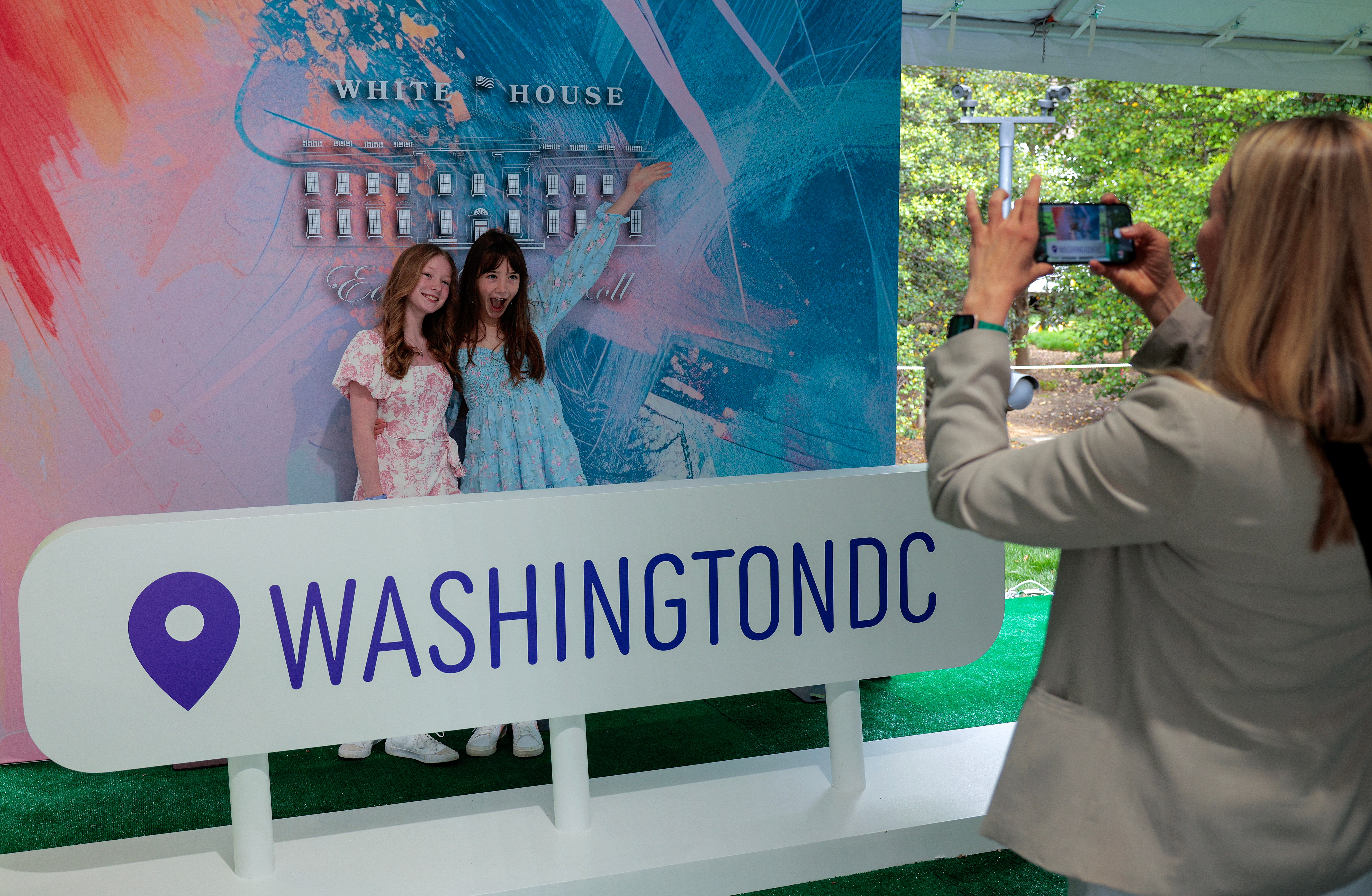 女性二人が「WASHINGTON DC」と書かれた看板の前でポーズ。後ろには写真を撮る人がいる。