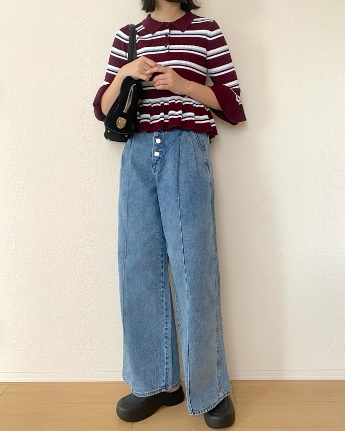 女性がストライプのトップスとデニムパンツ、プラットフォームシューズを着用し、バッグを持っている全身写真。