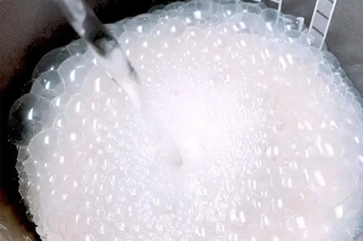 炊飯器の中に水を注いでいるシーン。米の周りに泡が立っている。