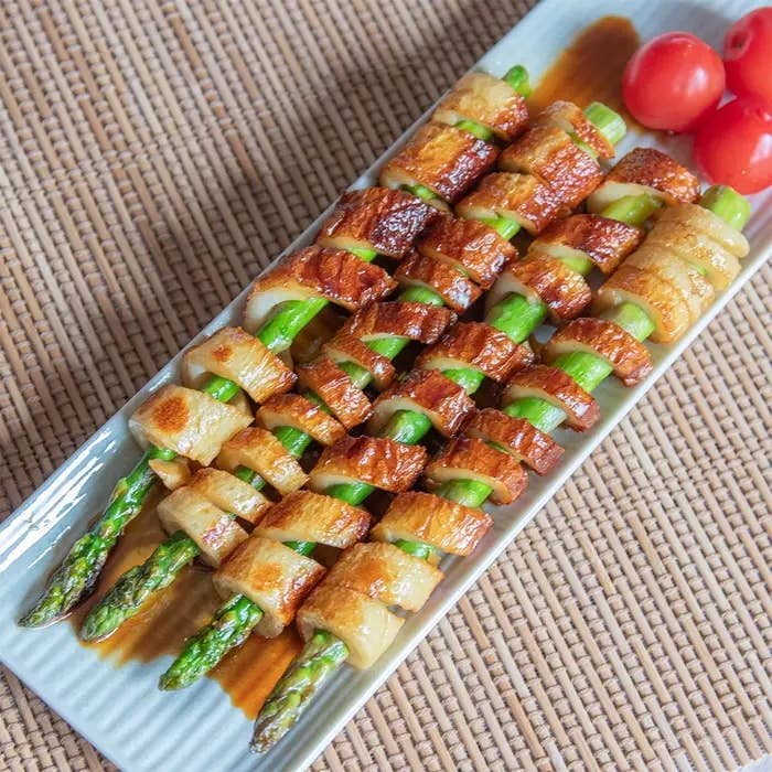 アスパラガスをちくわで巻いた料理が盛り付けられた皿。隣にミニトマトが添えられている。