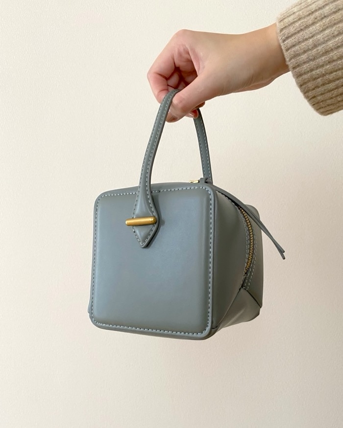 Hand holding a small, minimalist handbag with a cube shape and sleek design