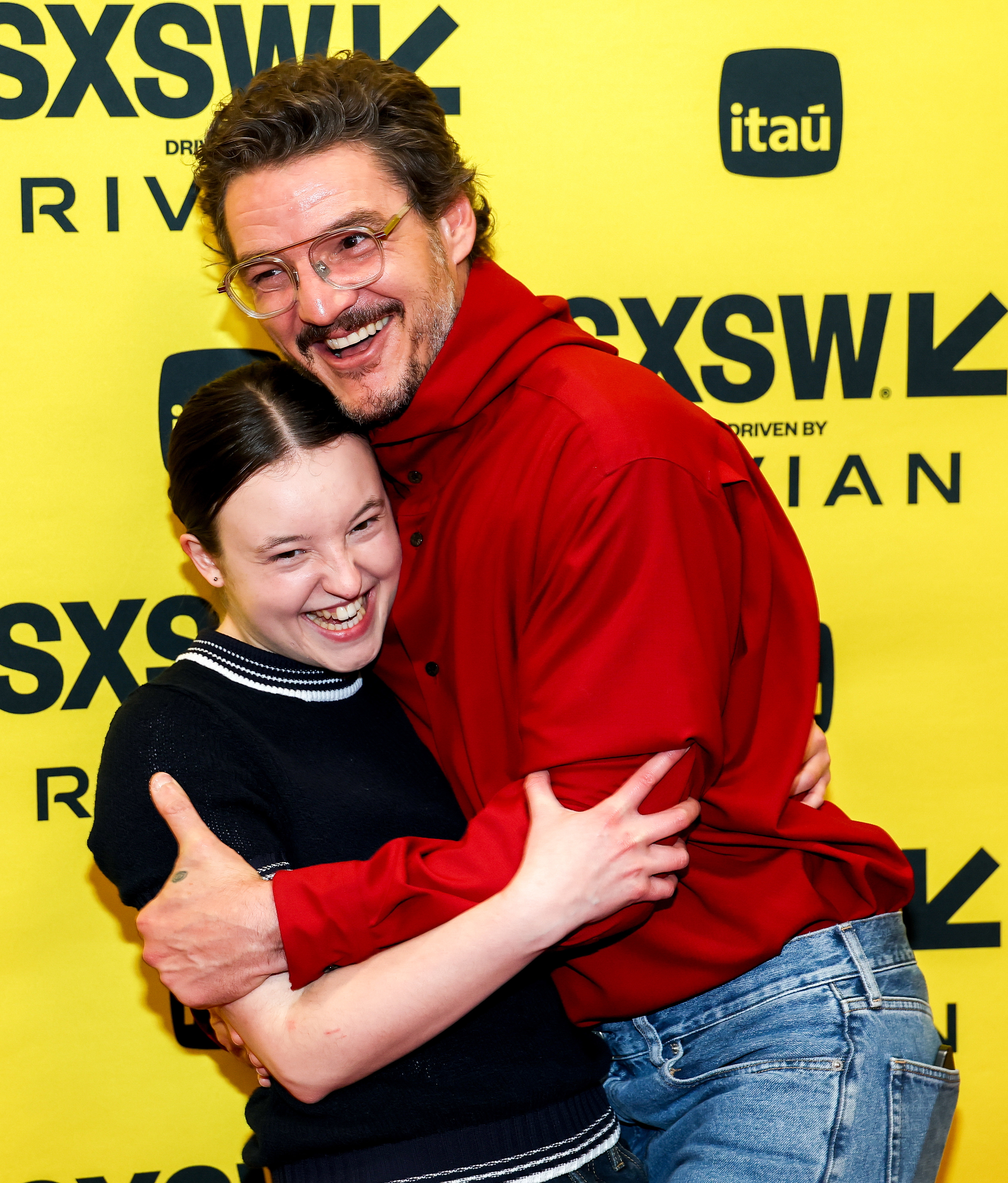 Bella Ramsey and Pedro Pascal laughing and hugging each other on a red carpet