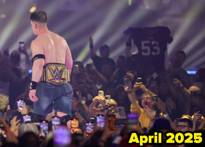 Wrestler in a ring with championship belt, facing a cheering crowd with phones up, capturing the moment at a lively event
