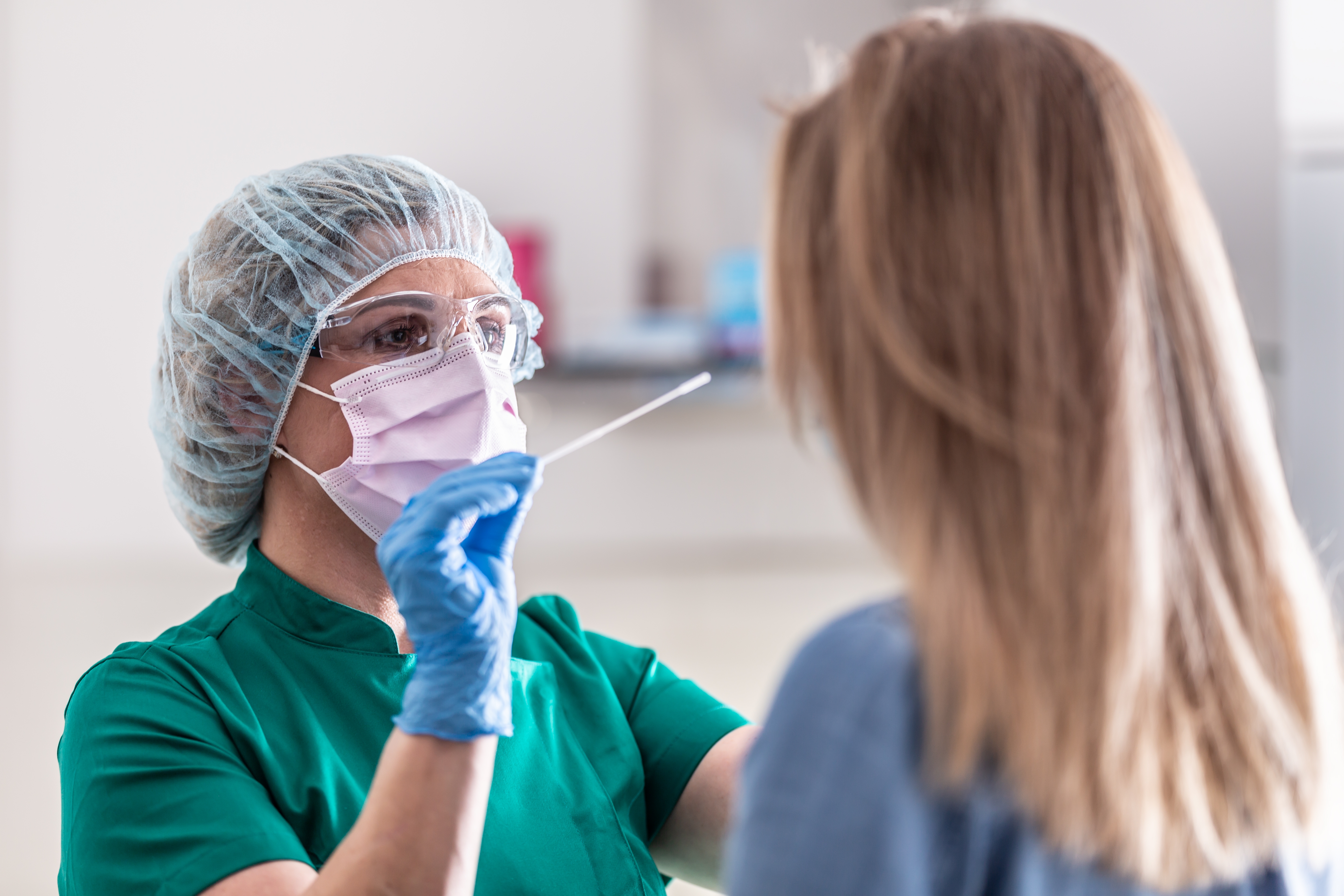 Healthcare worker in protective gear performing a COVID-19 test on a patient with long hair