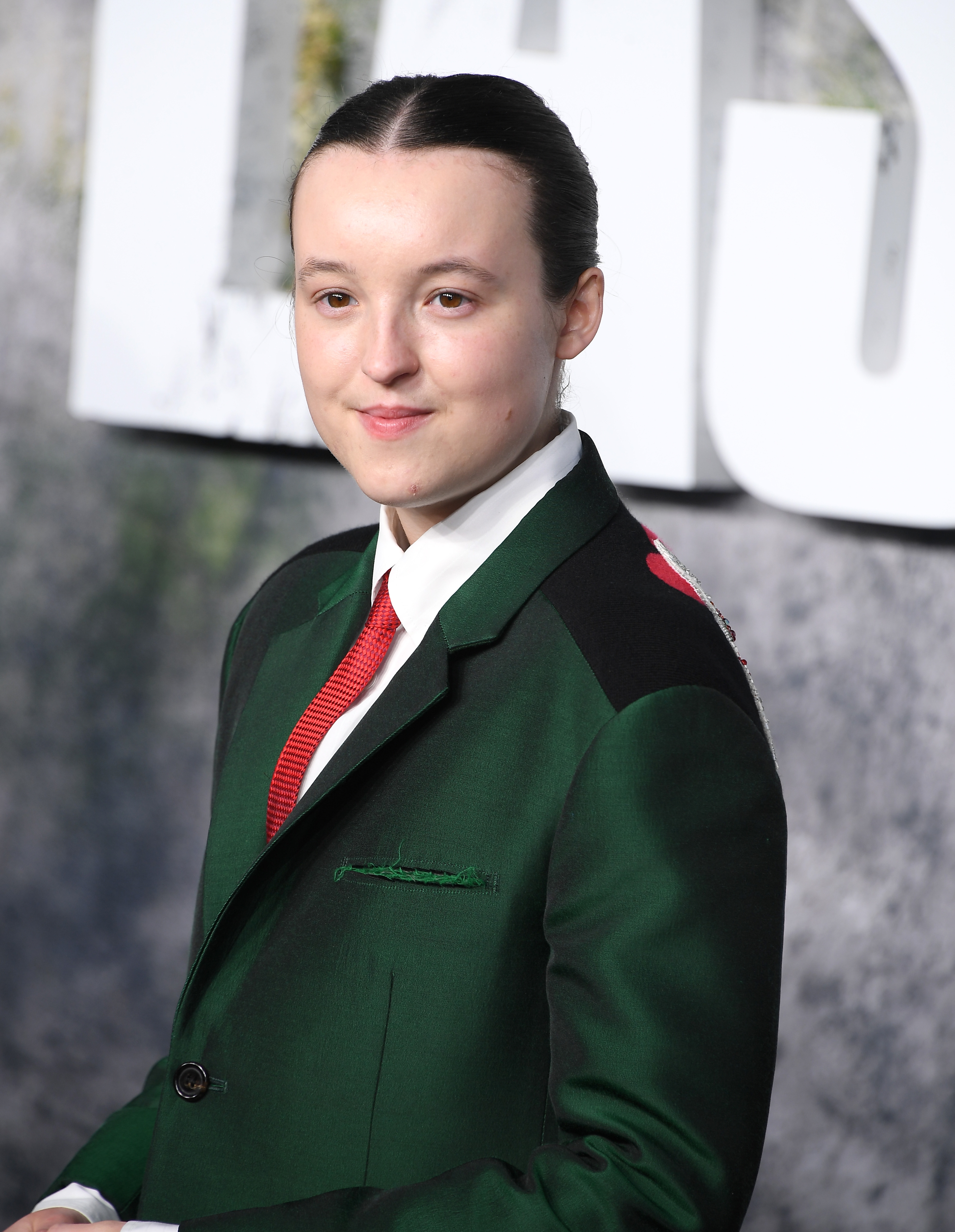Bella in a tailored suit with a red tie on a red carpet at an event, smiling with hair pulled back
