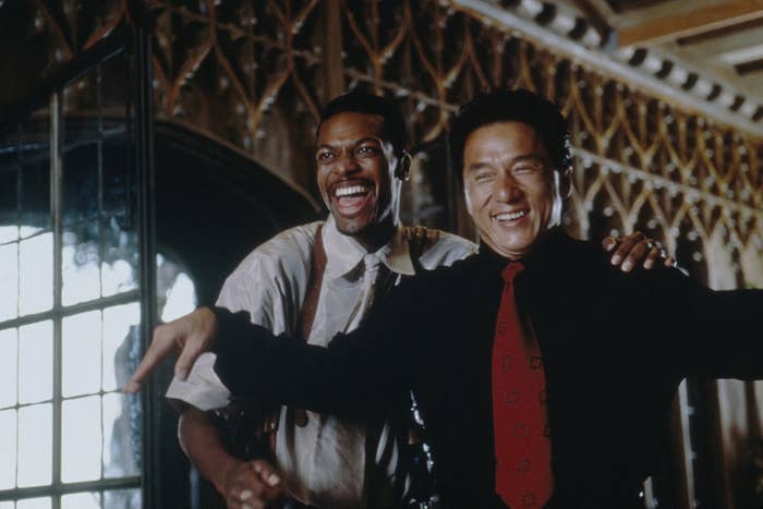 Two men laughing together, one wearing a white shirt with suspenders and the other in a black shirt with a patterned red tie