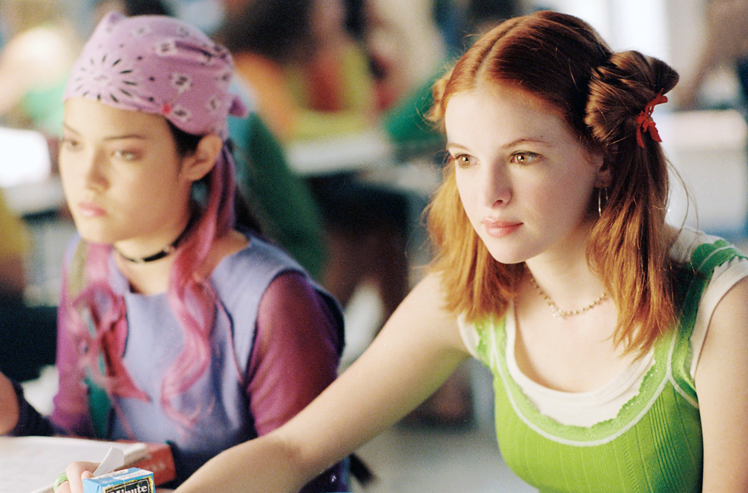 Two young women sit side by side, focused. One wears a patterned bandana, and the other has styled hair with small buns