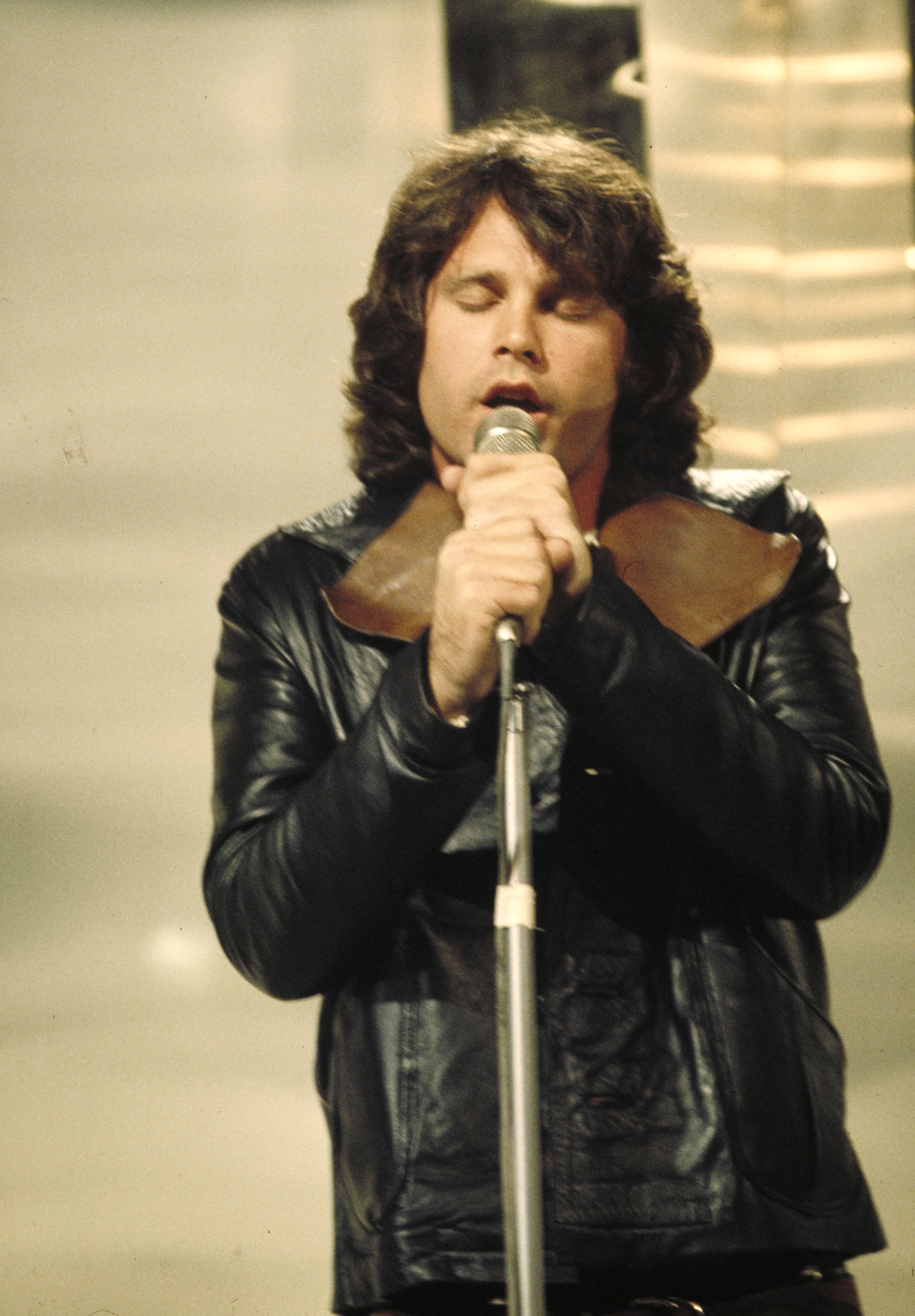Person in a black leather jacket sings passionately into a microphone on stage
