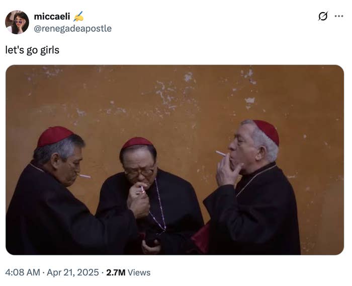 Three religious figures, in traditional robes and red caps, share a light for their cigarettes against an orange-brown wall