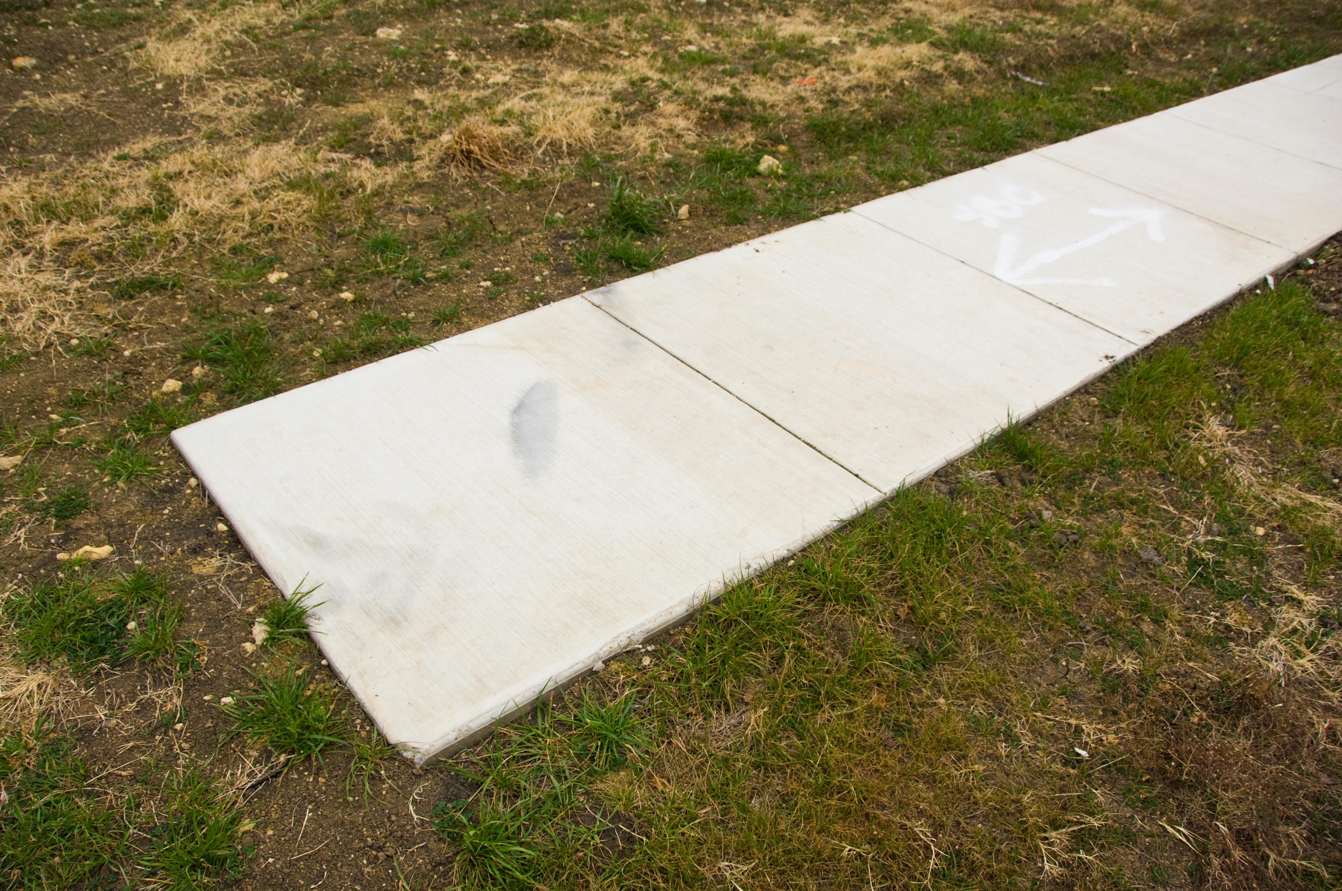 Uneven sidewalk with a noticeable drop-off at the end, adjacent to grass and dirt
