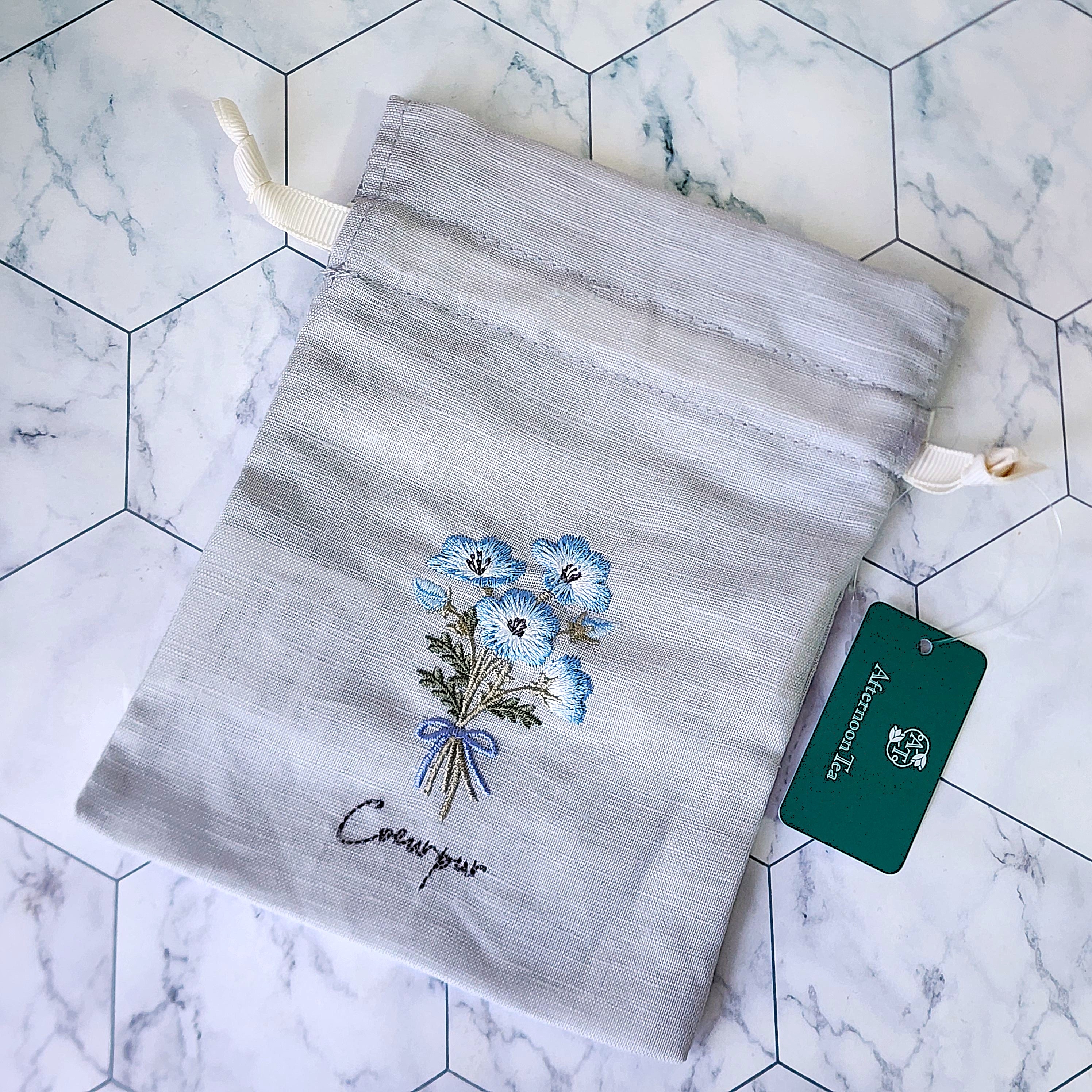 青い花が刺繍された灰色の布製バッグ。タグが付いています。