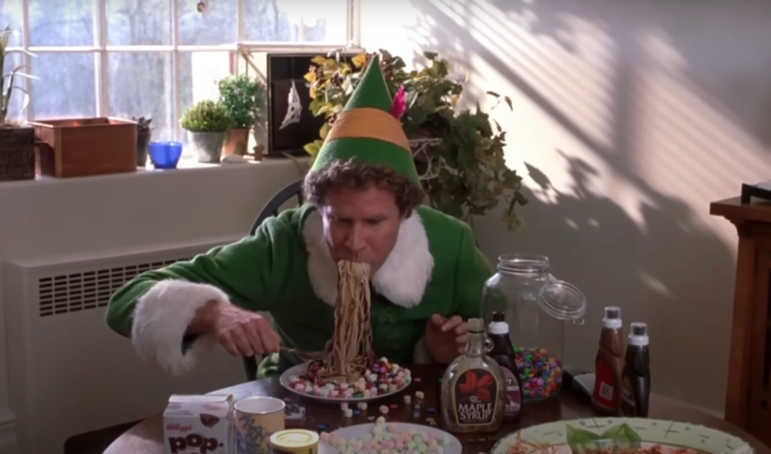 Buddy enthusiastically eats a plate of spaghetti mixed with syrup, candy, and breakfast items