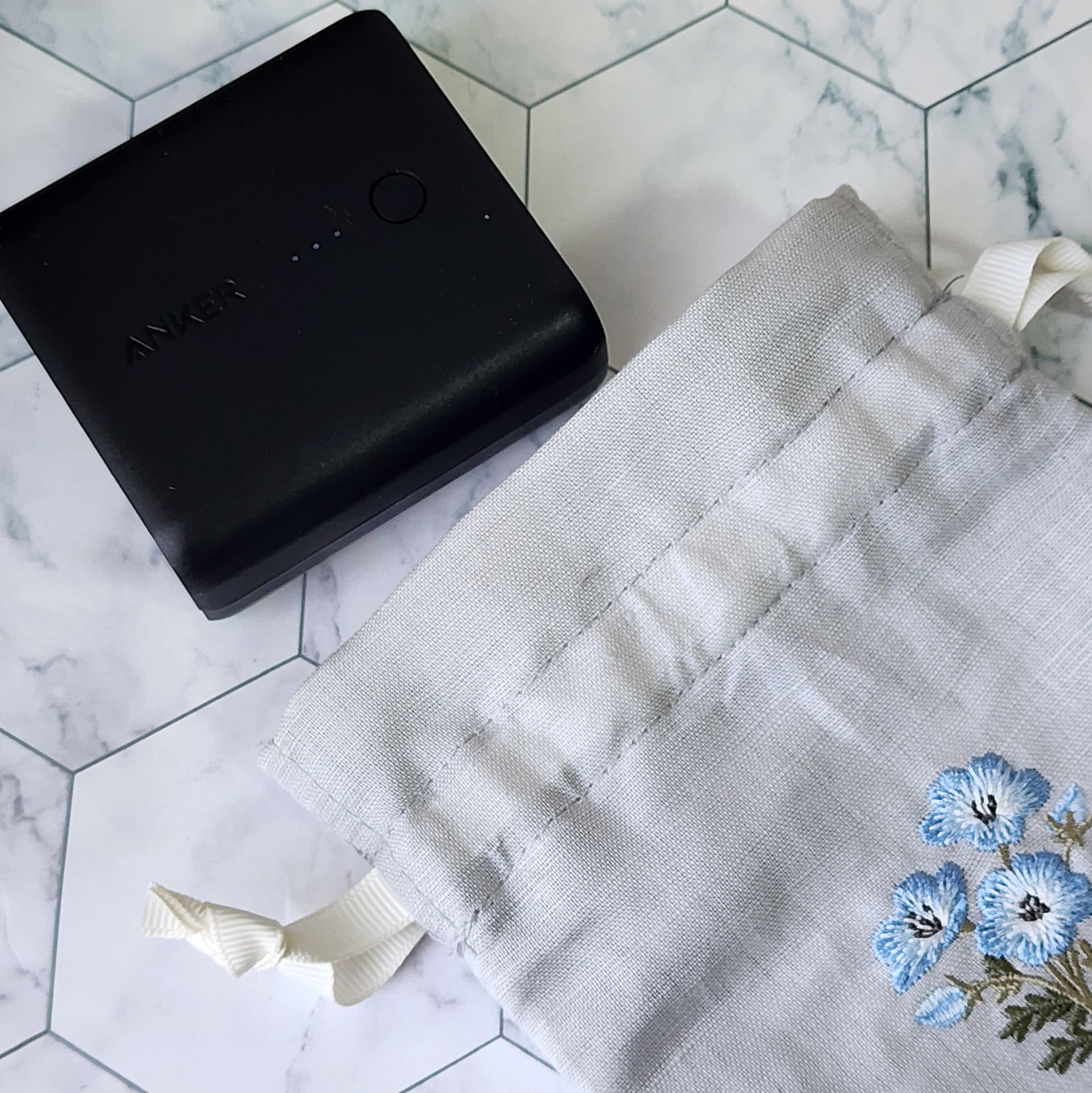 モバイル充電器と花柄の小物入れポーチが六角形模様の背景に置かれている。