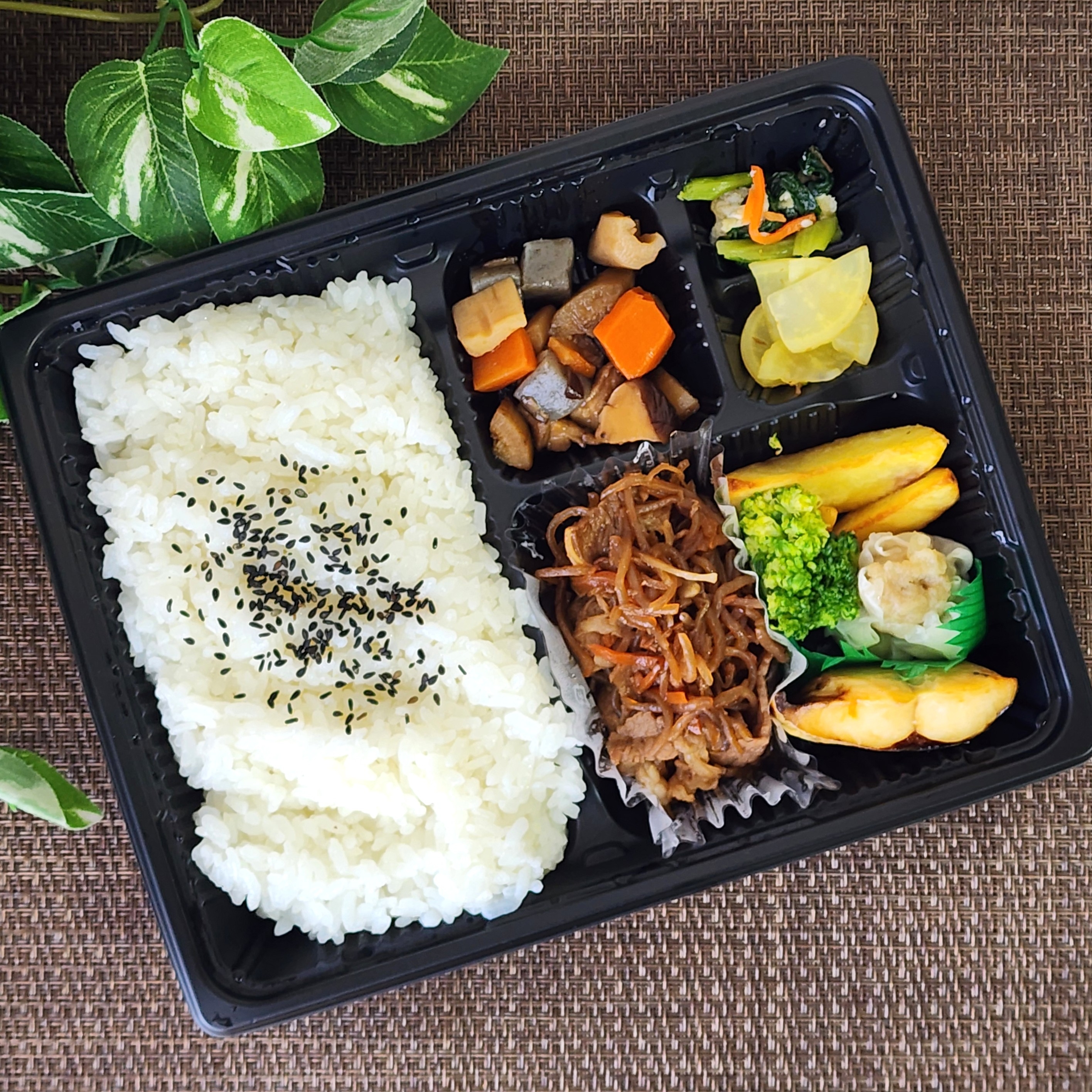 弁当箱に盛られたご飯と野菜、肉などのおかず。葉の装飾が見える。