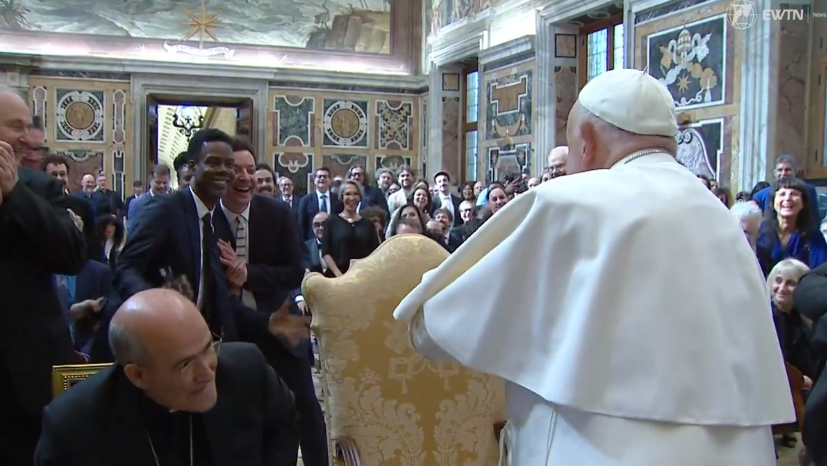 A smiling group meets a prominent religious leader dressed in traditional attire during a formal gathering in an elegant room