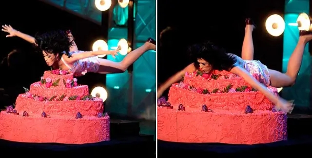 Person playfully dives into a large cake with decorative icing during a live performance
