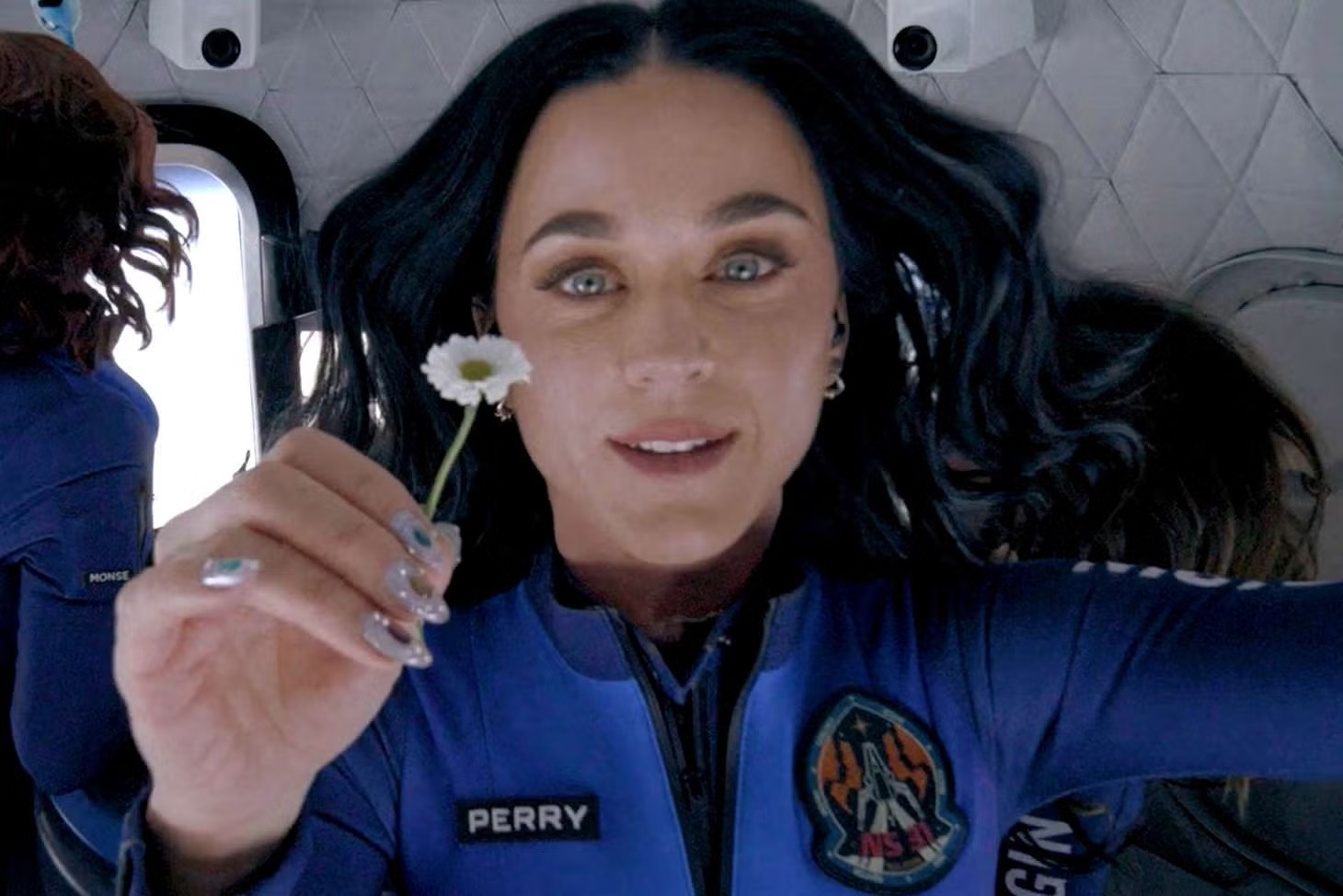 Person in a blue spacesuit floating in zero gravity, holding a small flower and smiling
