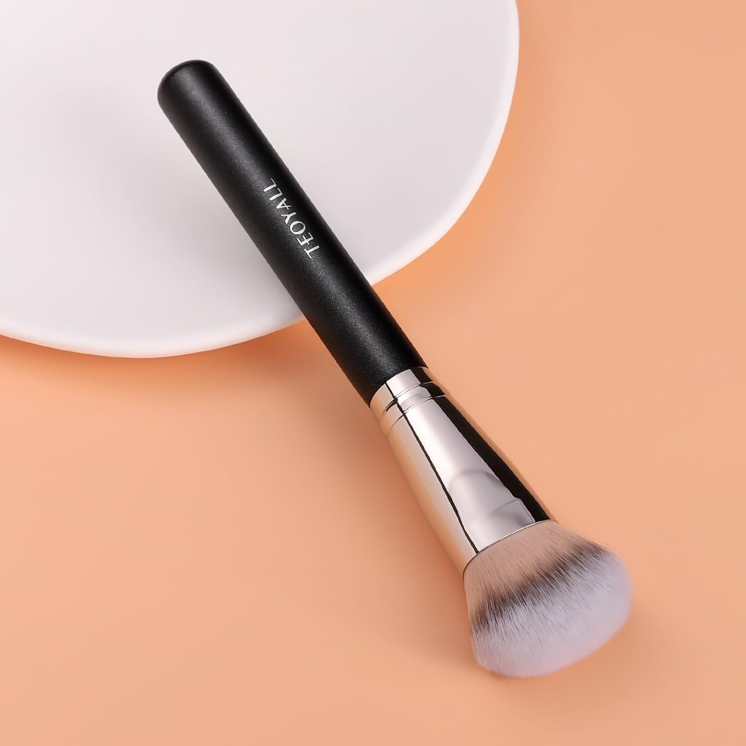 Makeup brush with a black handle and soft bristles, resting on a white surface