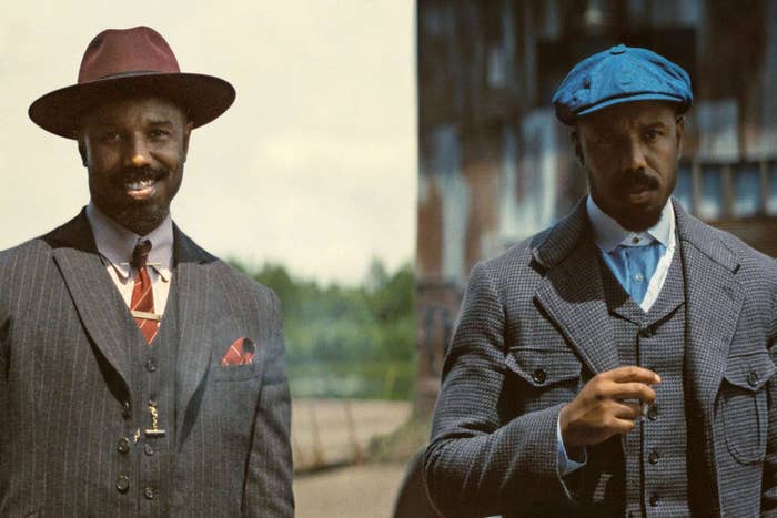 Dos hombres posan en atuendos retro. Uno lleva traje de rayas con sombrero; el otro, traje cruzado con gorra. Ambos tienen expresión seria