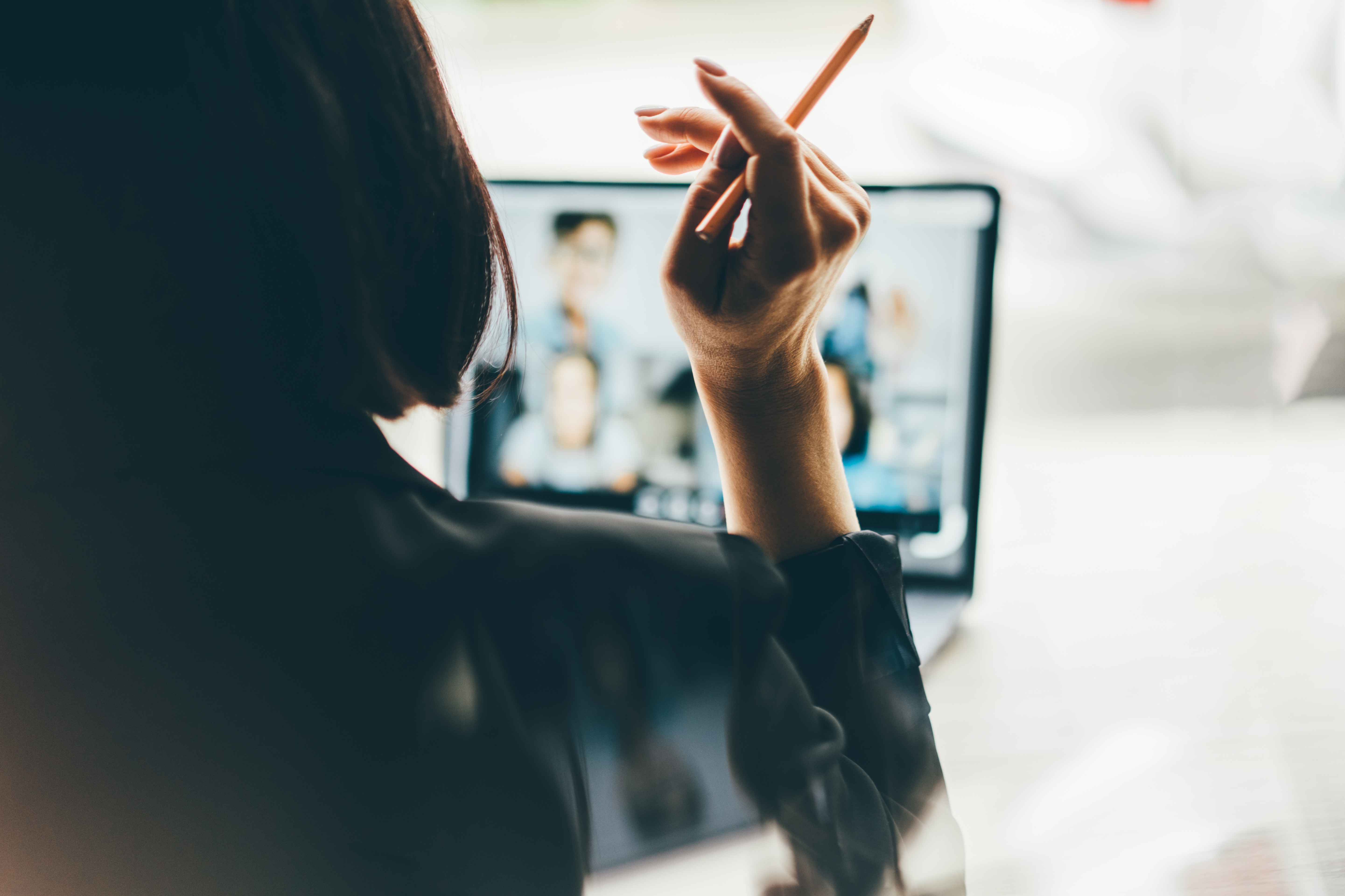 Person with short hair holds pencil, looking at a computer screen displaying multiple blurred images, suggesting a creative or analytical task