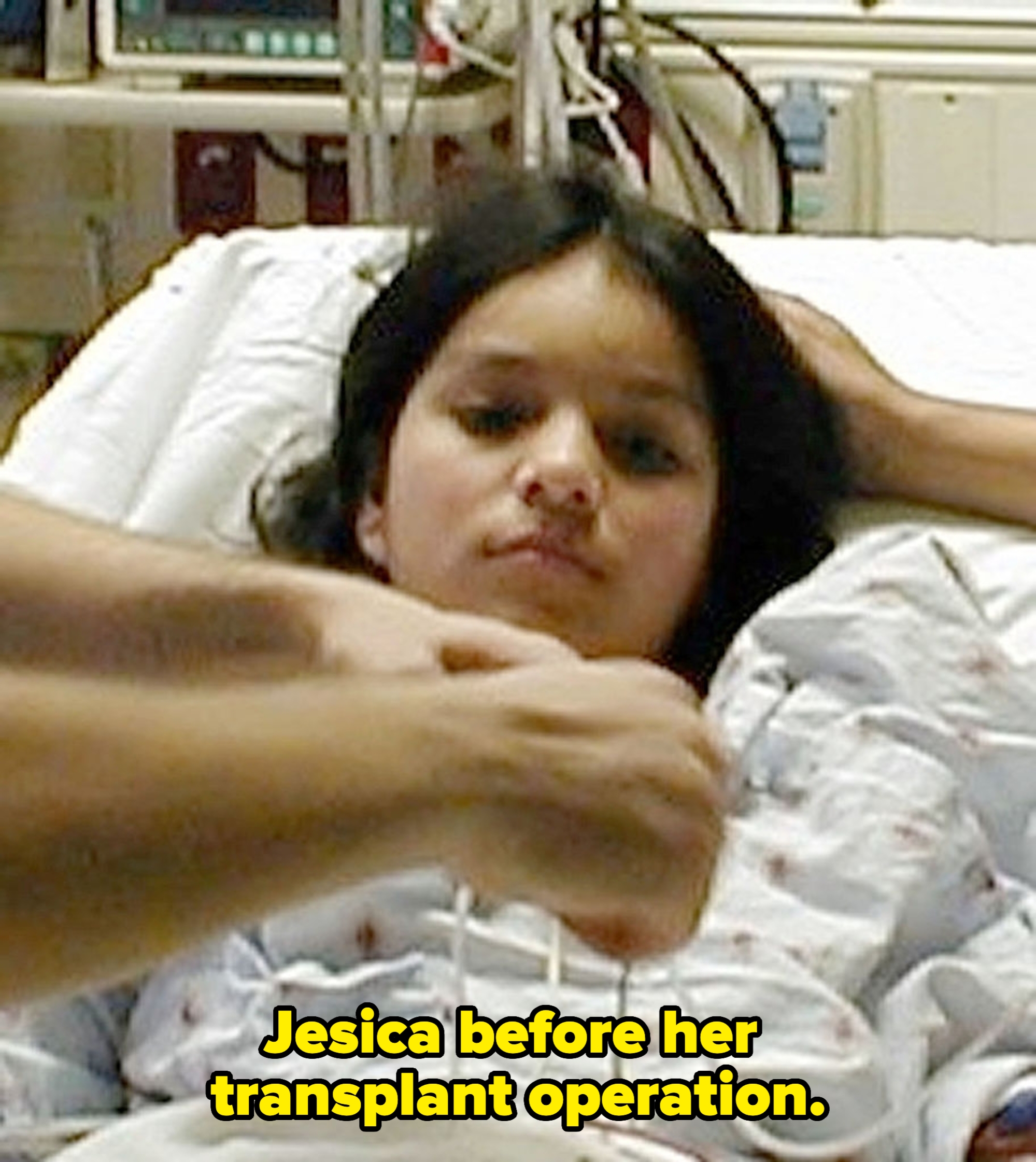 Person in hospital bed receiving medical attention, appearing calm. Medical equipment visible in the background