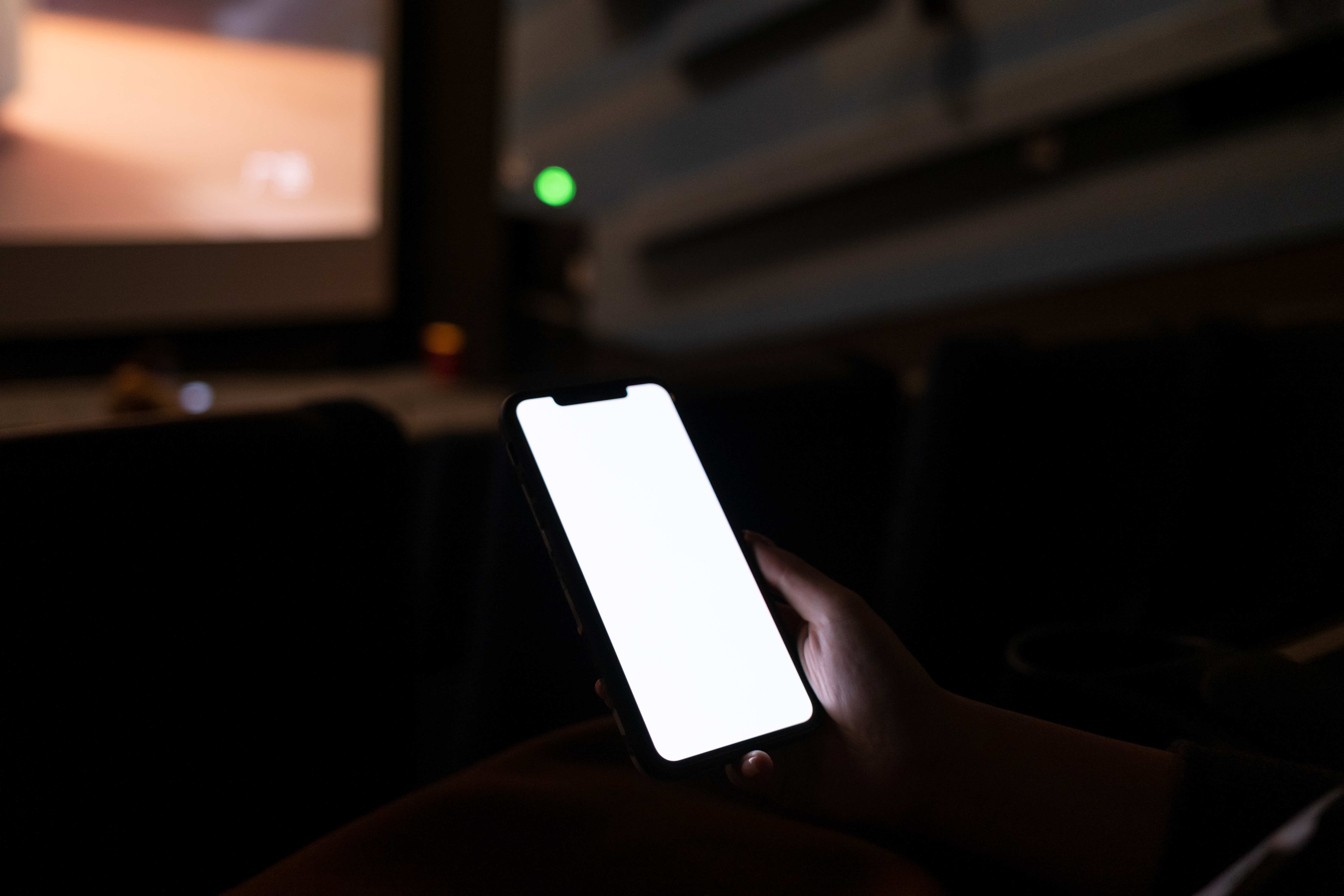 Person holds a glowing phone in a dimly lit theater with an empty screen