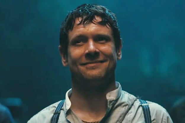 Hombre sonriente con camisa blanca y tirantes en un entorno oscuro