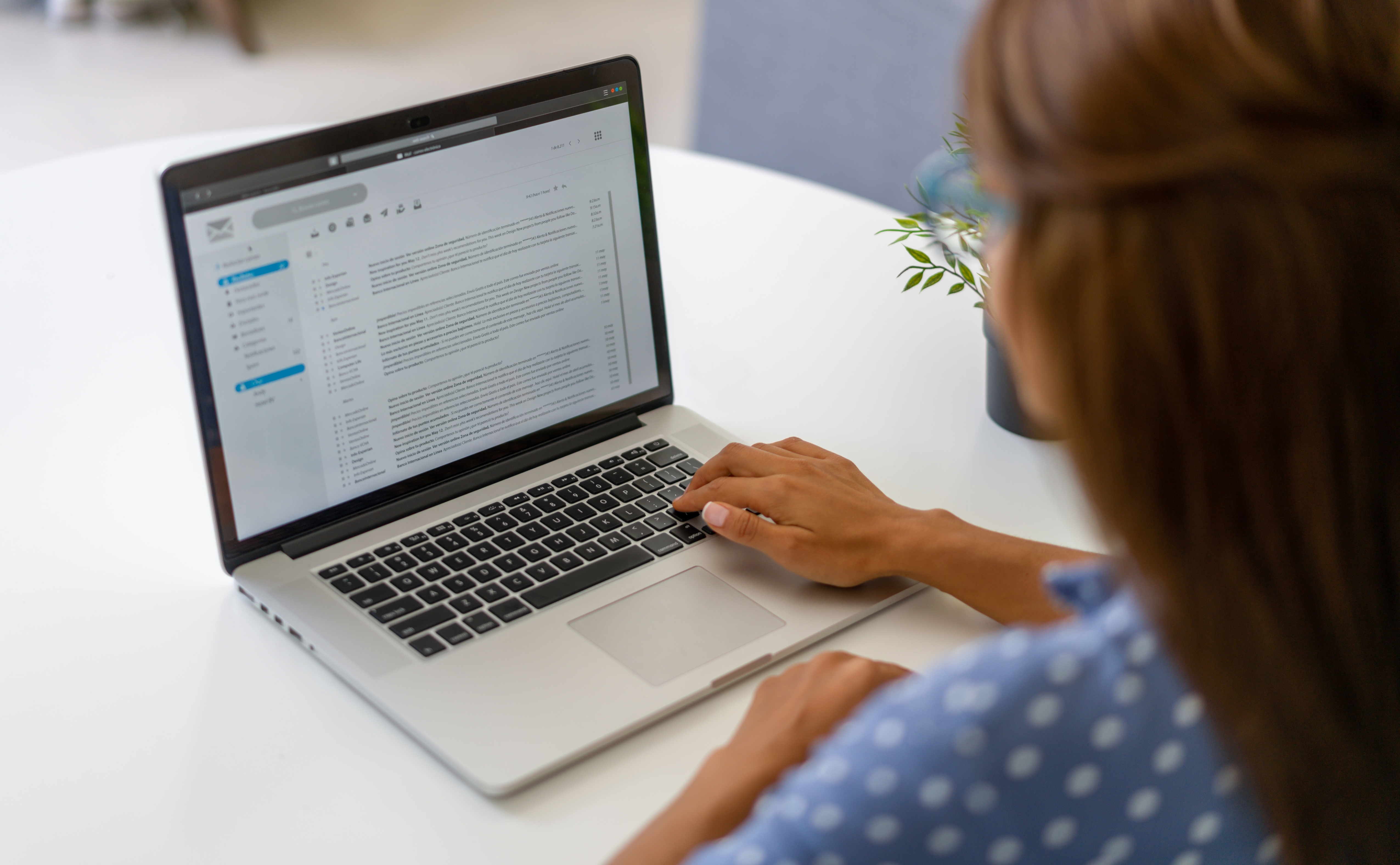 Person in polka dot blouse using a laptop at a table, focused on reading or typing an email