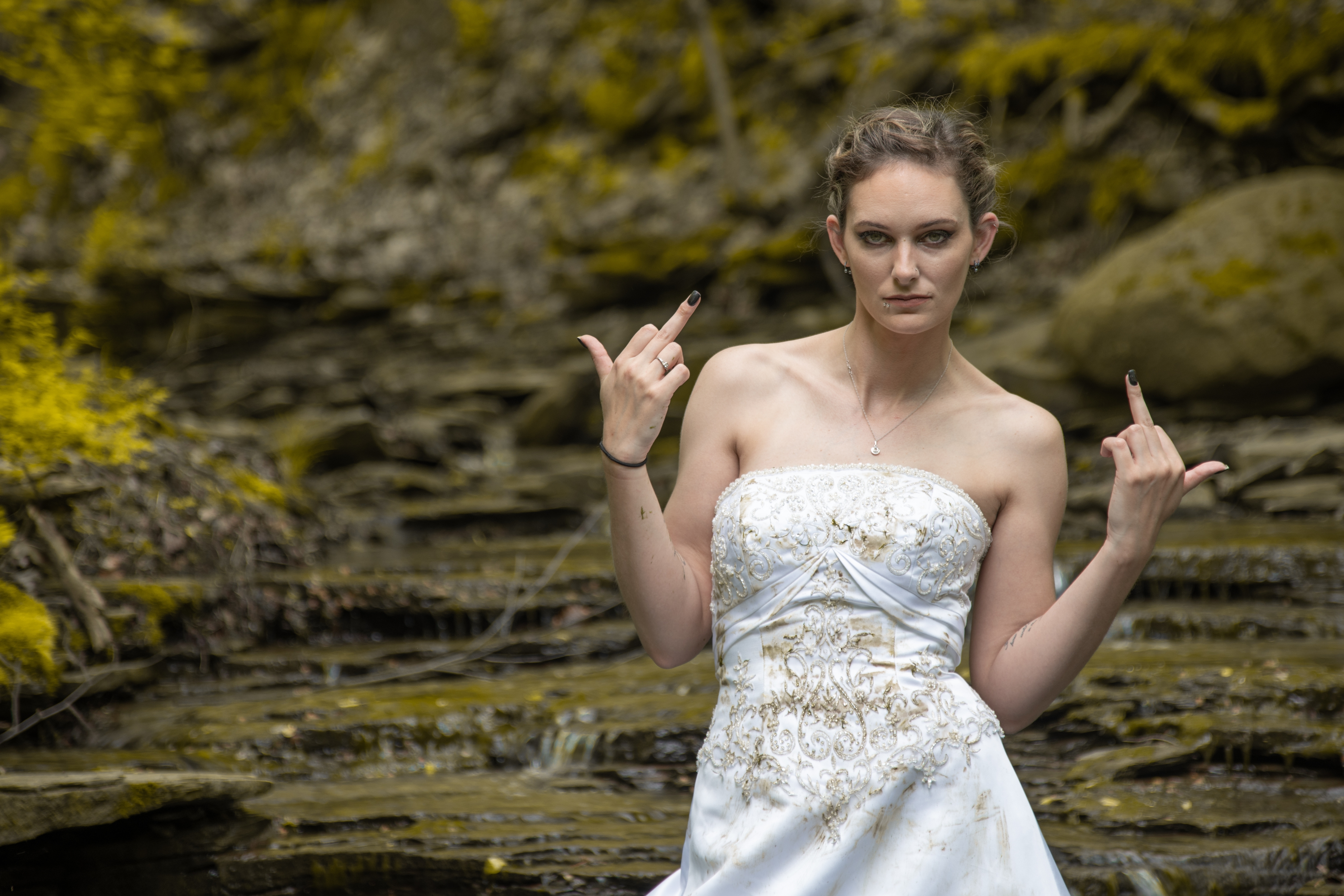 Person wearing an embroidered strapless dress, standing outdoors, making a bold gesture with both hands