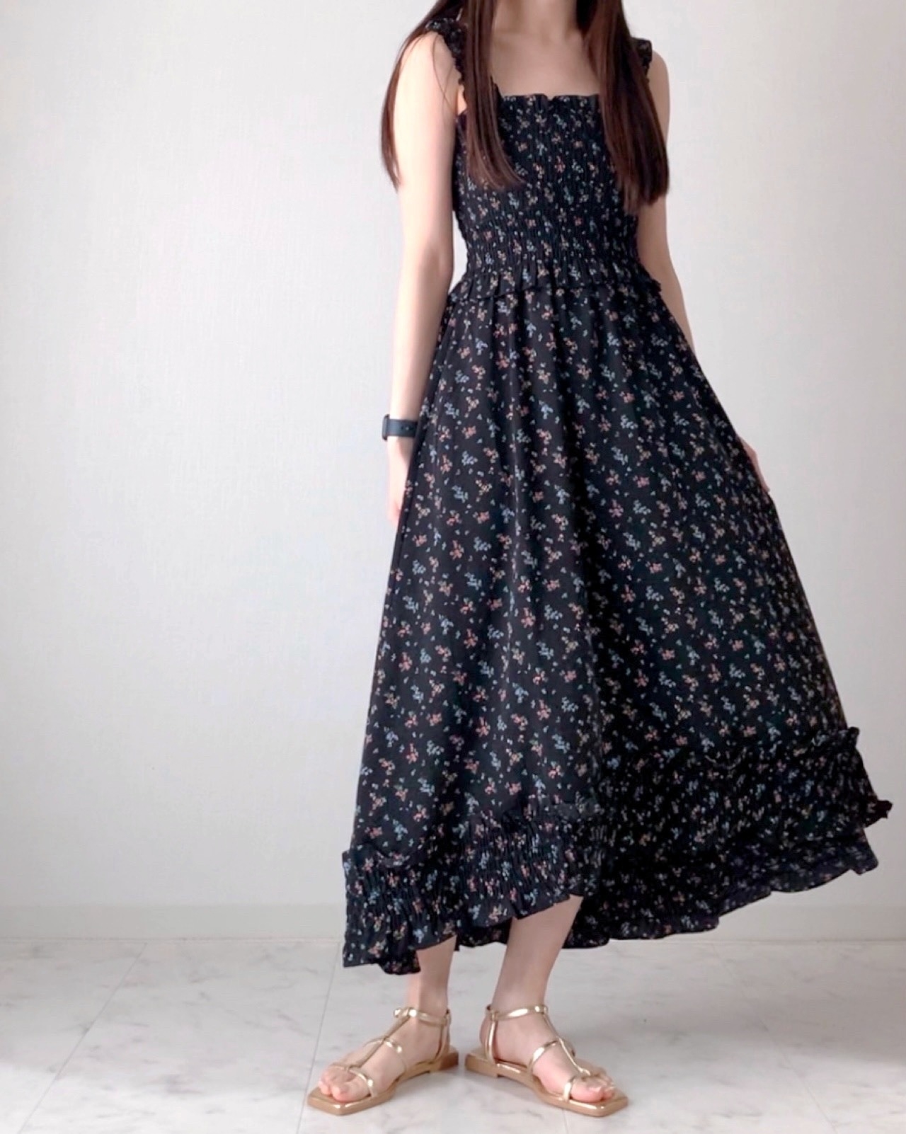 女性が花柄のロングワンピースとサンダルを着用しポーズをとっている。