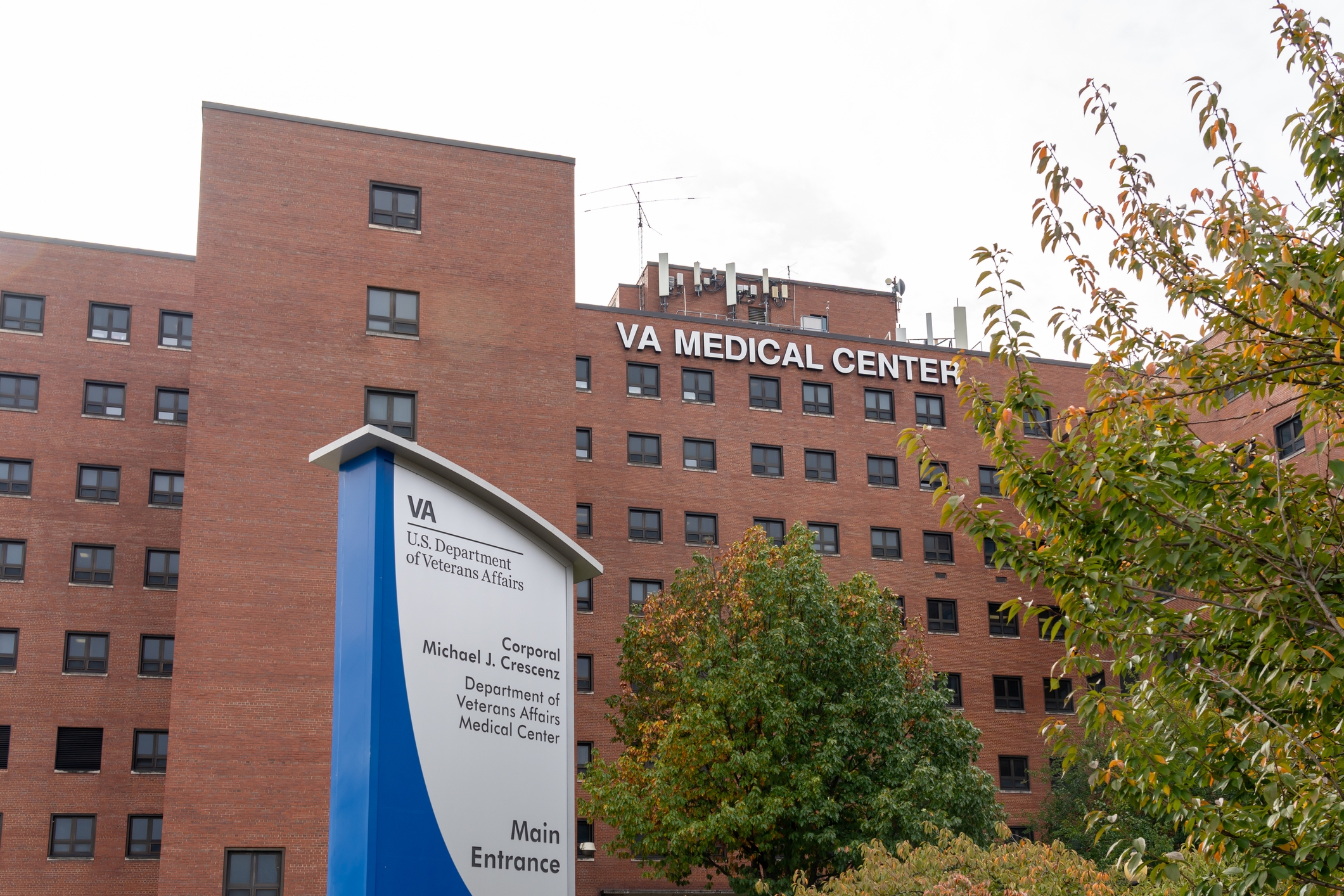 Exterior view of a large VA Medical Center building with a prominent entrance sign in front, surrounded by trees