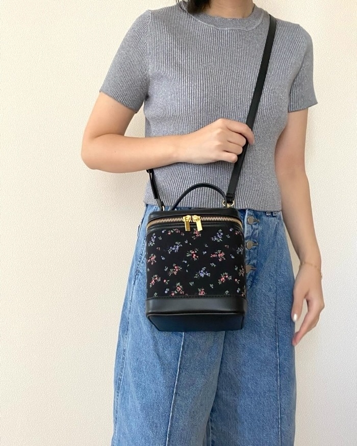 女性が花柄のショルダーバッグを持ち、リラックスしたカジュアルスタイルで立っている。