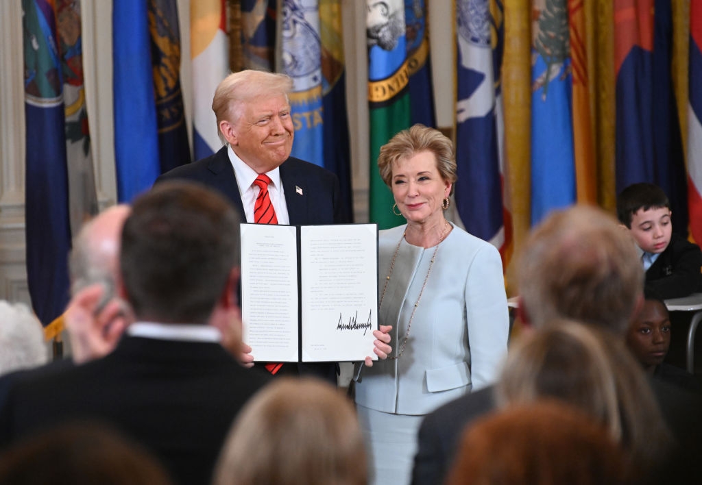 Two people stand together holding a signed document at an official event, surrounded by an audience