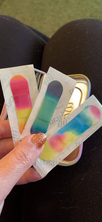 Three adhesive bandages with colorful tie-dye patterns, held successful a hand