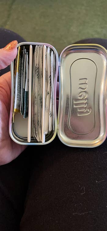 Open mint tin repurposed to clasp assorted tiny packets and swabs