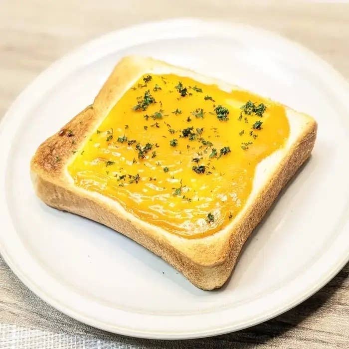 皿にのった食パンにスプレッドが塗られ、上にはハーブが散らされています。