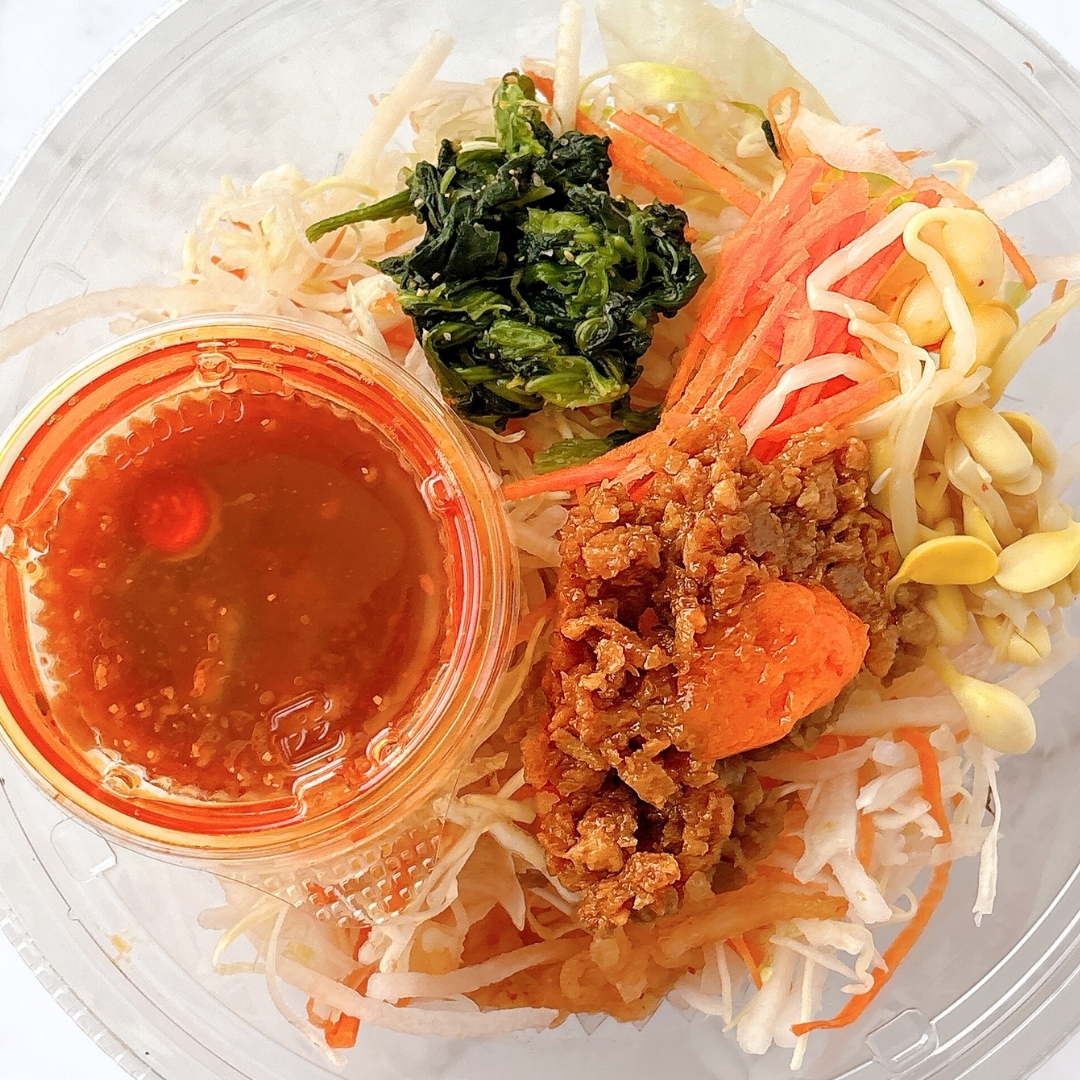 プラスチック容器に、にんじん、もやし、ほうれん草と共にドレッシングカップが入った野菜サラダ。