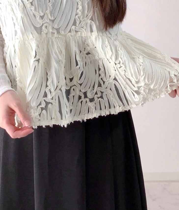 Person showing a white textured top with artistic patterns over a dark skirt, highlighting the garment's intricate details