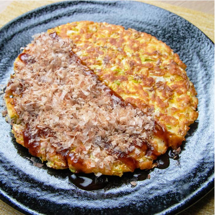 大きな黒い皿に盛られたトッピング付きのお好み焼き。試食、料理イベントの広告に使用。