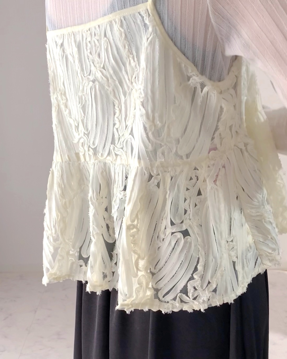 A person wearing a stylish lace top with a sheer, flowing design paired with a dark skirt