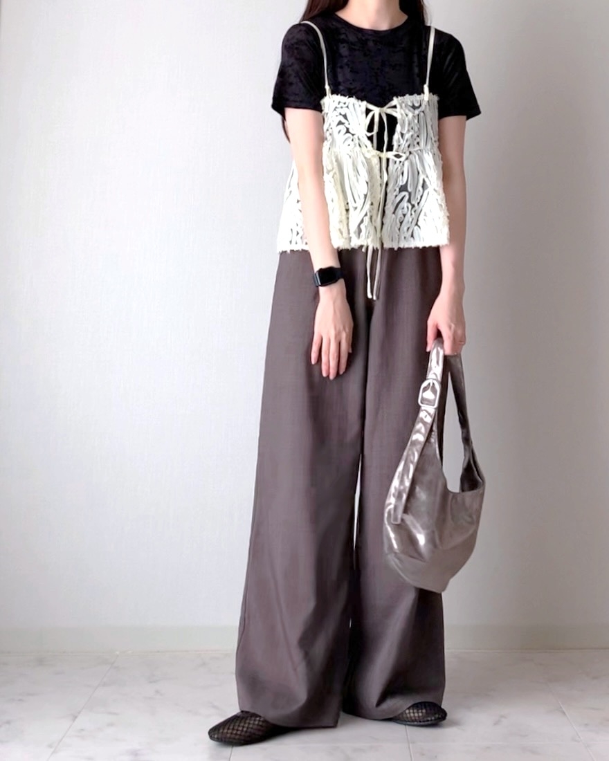 Person in wide-legged trousers, lace tank top over black shirt, holding a metallic purse. Fashion-forward casual style