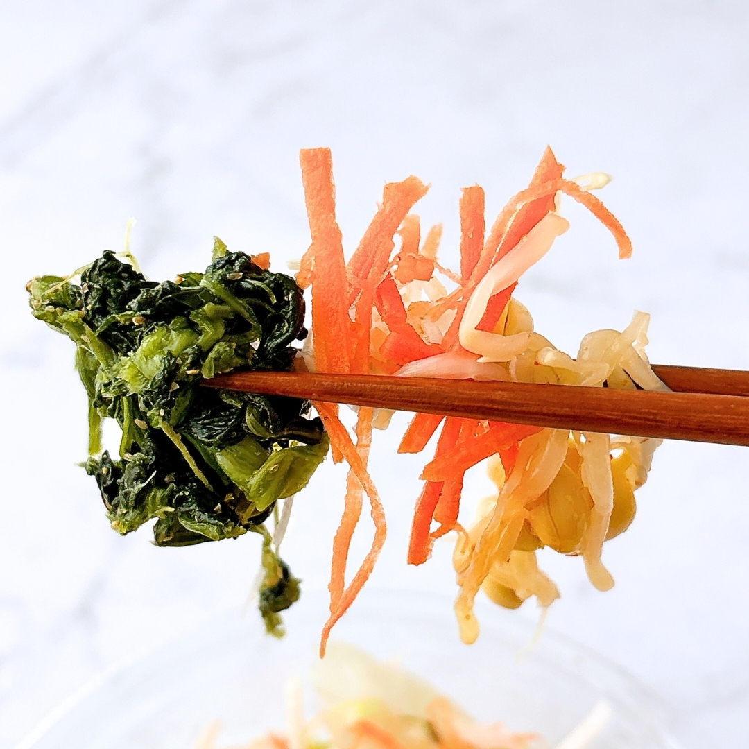 箸で持ち上げられた野菜の束。野菜には、ニンジン、もやし、緑の葉物が含まれている。