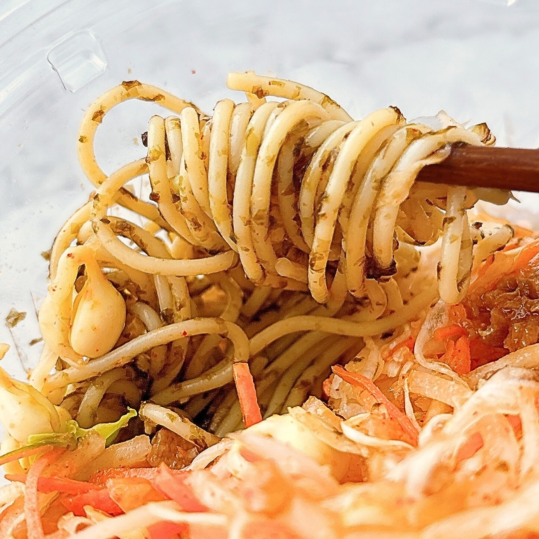 箸で持ち上げられた麺料理。にんにくや野菜がトッピングされている。