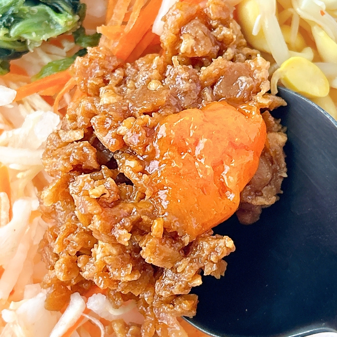 ビビンバの上に乗った甘辛い味噌と野菜のクローズアップ。黒いスプーンが横に添えられている。