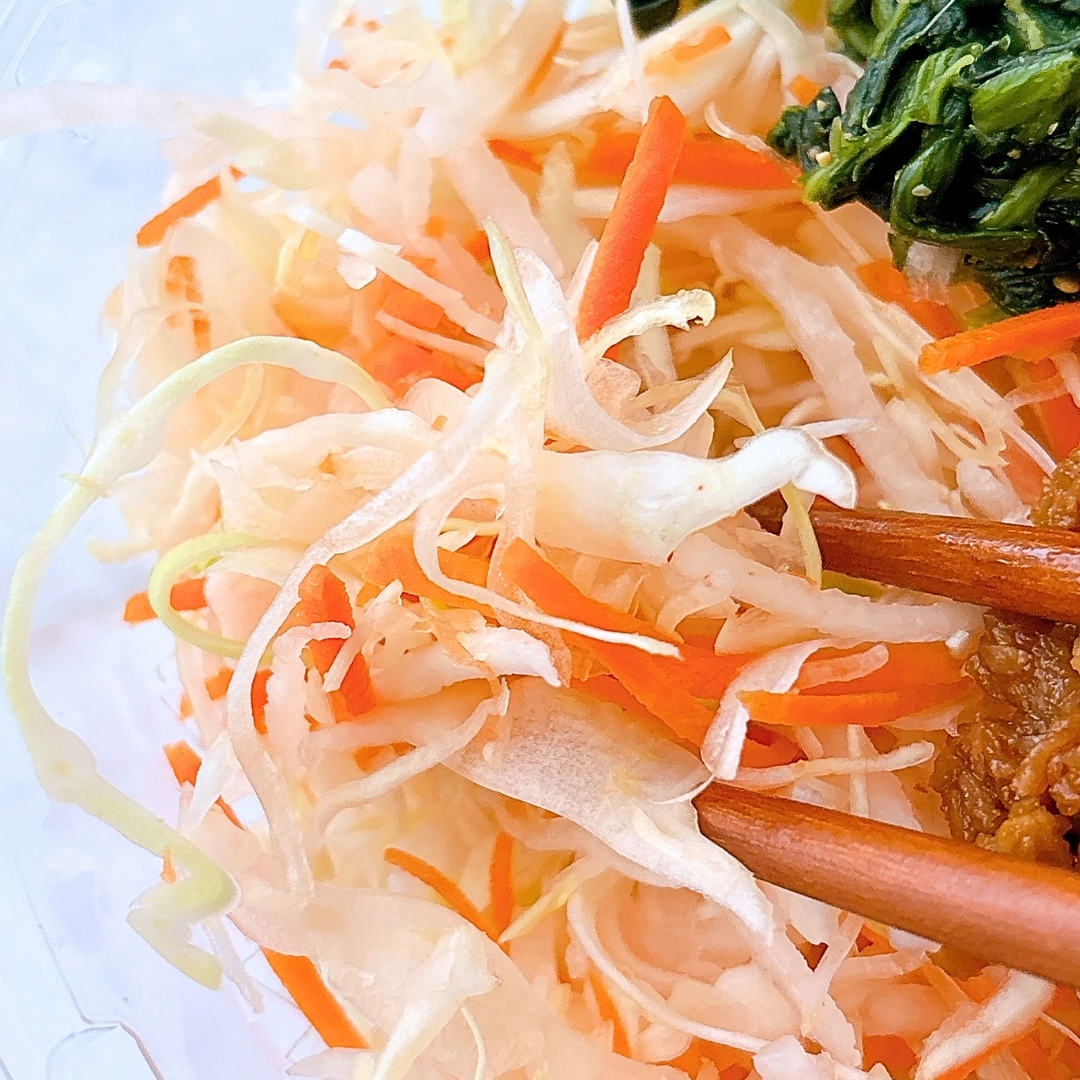 千切りキャベツとニンジンのサラダと箸でつまんだ肉料理。