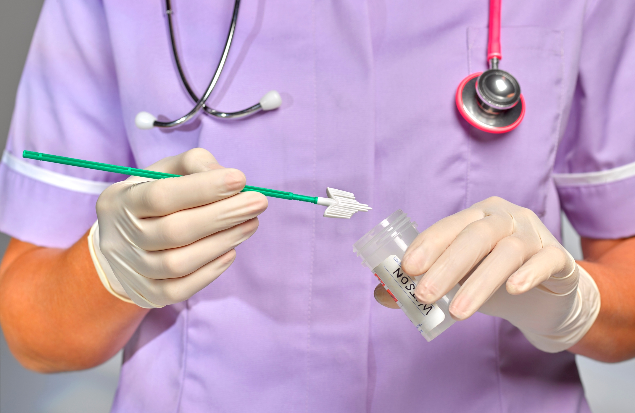 Healthcare worker holding Pap smear brush and sample container with gloves and stethoscope