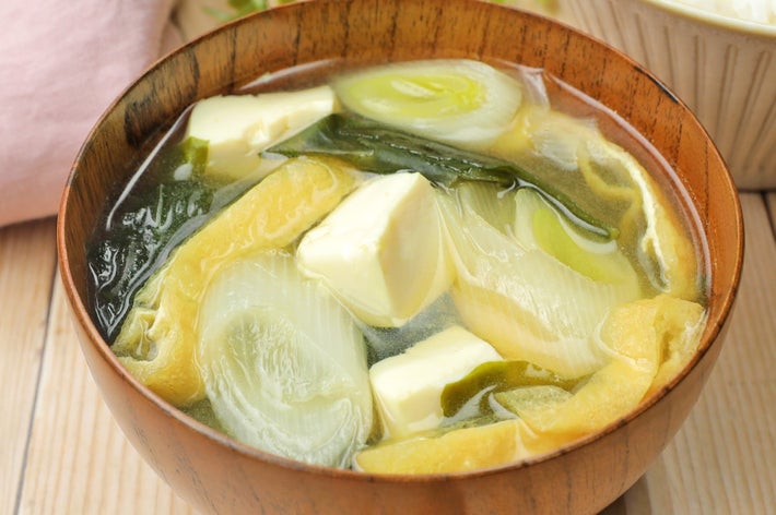 木の器に盛られたみそ汁。豆腐、ネギ、わかめが入っている。背景にご飯。