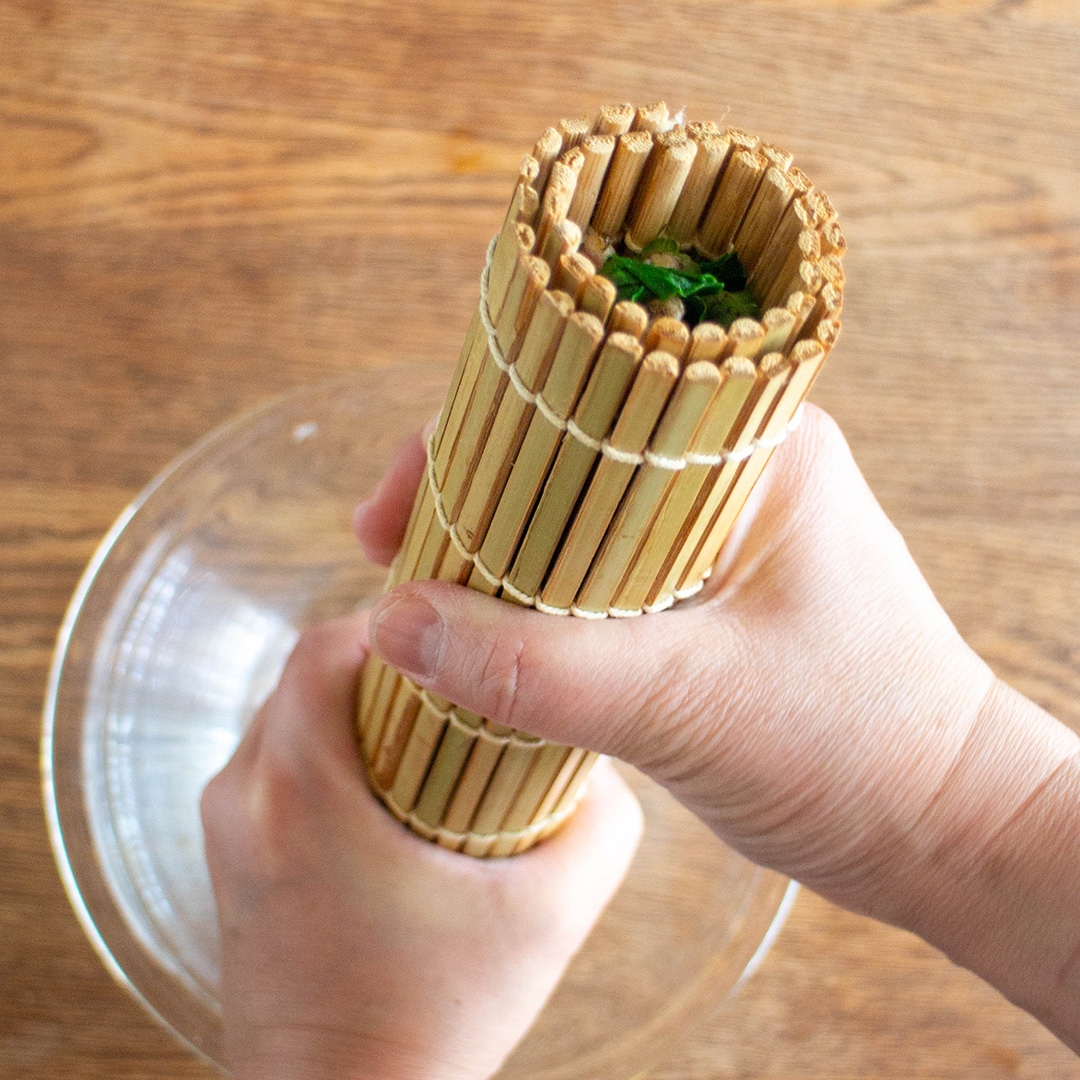 手で竹製のすだれを握り、中に何かを詰め込んでいる様子が写っています。