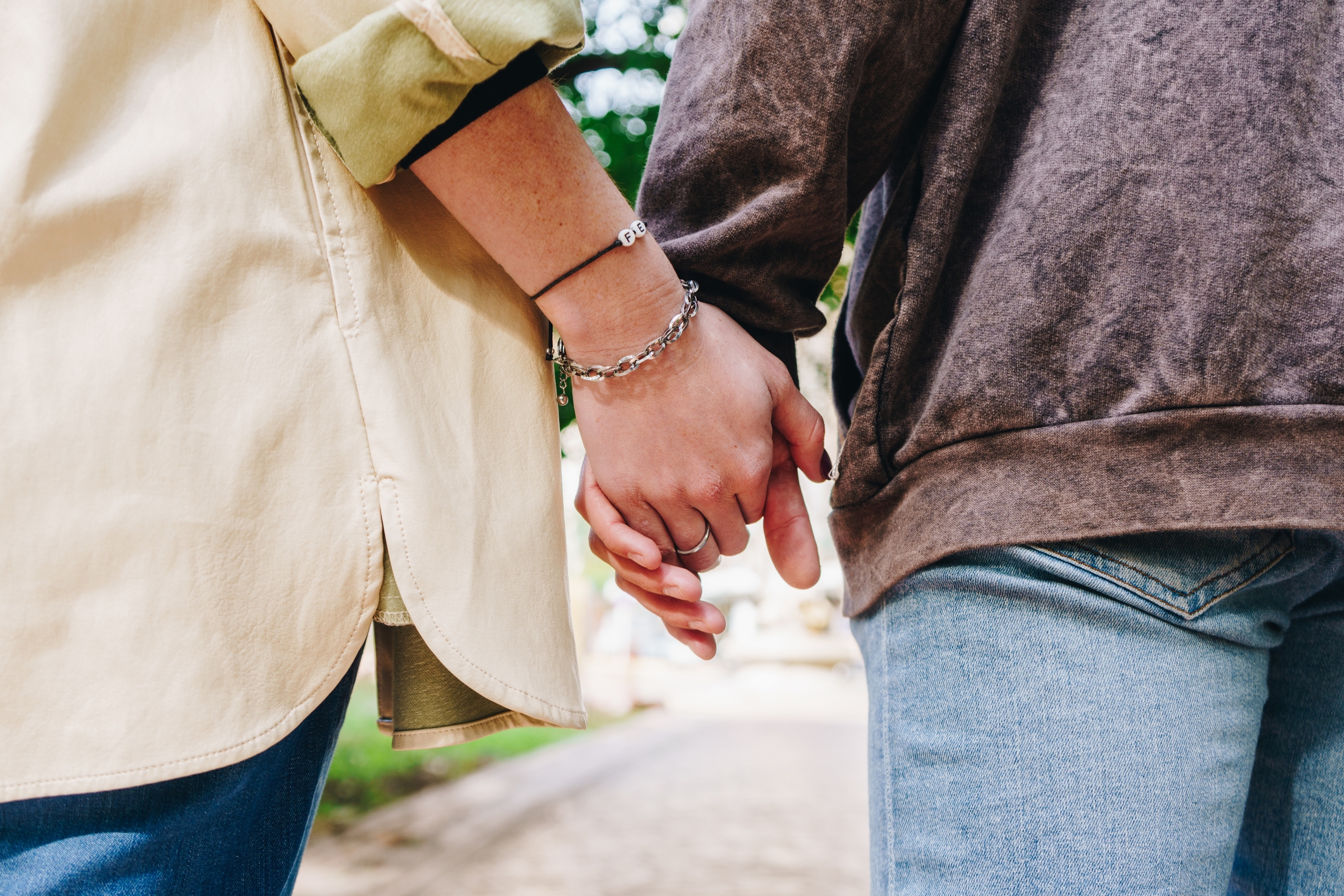 Two people holding hands outdoors, wearing casual long-sleeve shirts and jeans, showcasing a moment of connection and togetherness